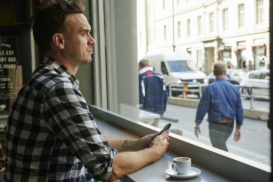 Sweden, Man holding cellphone and looking through window in cafe