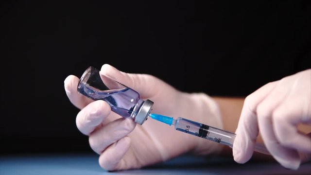 Close up mixing of medicine in ampoule. Vial and syringe in doctor's hands. Hands in white gloves