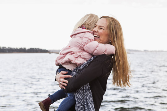 Solvesborg, Blekinge, Sweden, Mid adult woman holding girl (2-3) at seashore