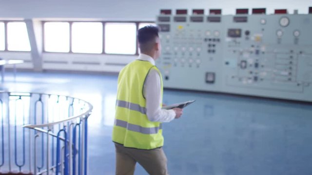 Workers in power plant control room looking at control panel & checking system