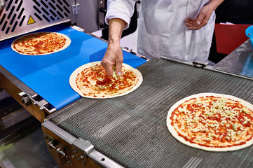 Worker cook adds cheese to pizza on conveyor