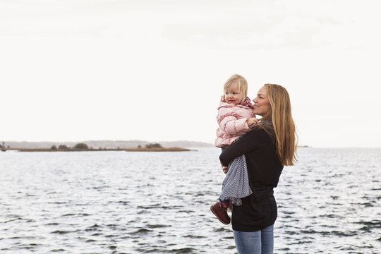 Solvesborg, Blekinge, Sweden, Mid adult woman holding girl (2-3) at seashore