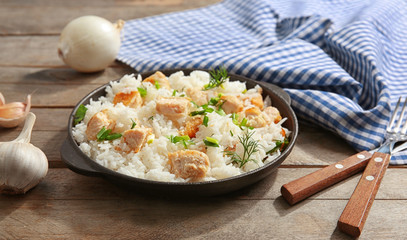 Delicious rice with chicken in pan on wooden table
