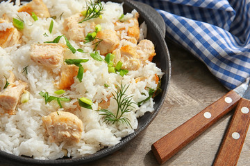 Delicious rice with chicken in pan on wooden table