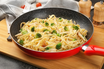 Frying pan with delicious chicken Alfredo on wooden board