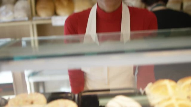  Friendly worker in bakery shop serving customer at the counter