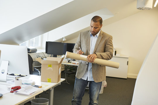 Sweden, Businessman writing note on paper tube in office