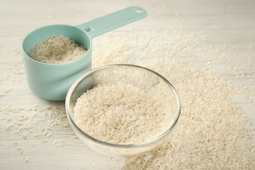 Lot of rice in bowl and measuring scoop on wooden table