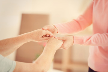 Old and young women holding hands on blurred background, closeup