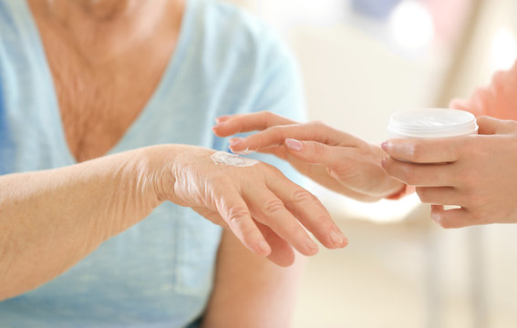 Woman applying cream on hand of elderly patient