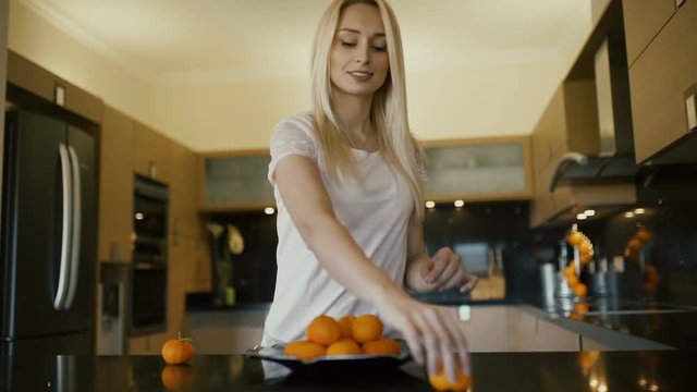 Beautiful blonde making a pyramide with oranges on the kitchen