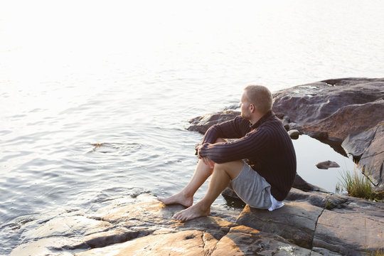 Sweden, Stockholm Archipelago, Sodermanland, Orno, Mature man sitting on rocky lakeshore