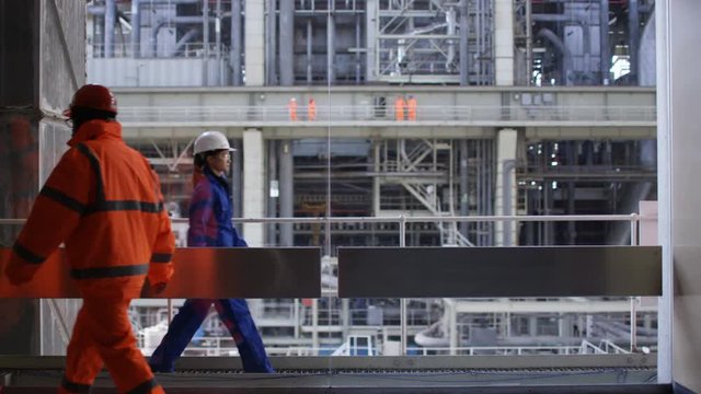  Female engineer talking on radio at power plant with colleagues walking by