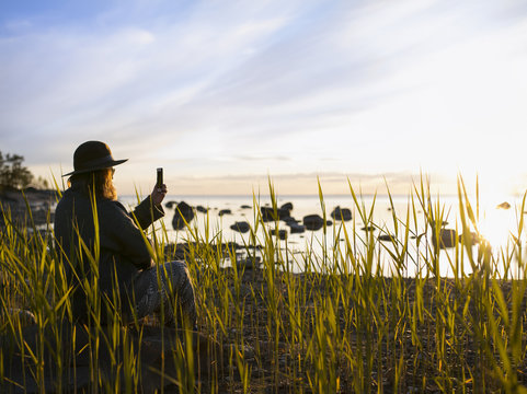 Finland, Ostrobothnia, Jakobstad, Faboda, Woman sitting among reeds by sea and photographing