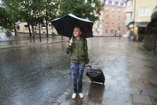 Sweden, Uppland, Solna, Resunda torg, Girl (10-11) carrying umbrella and pulling suitcase