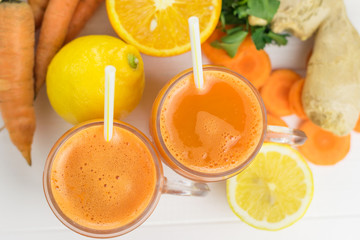 Two mugs with carrot smoothie with a straw on a white wooden table top view.