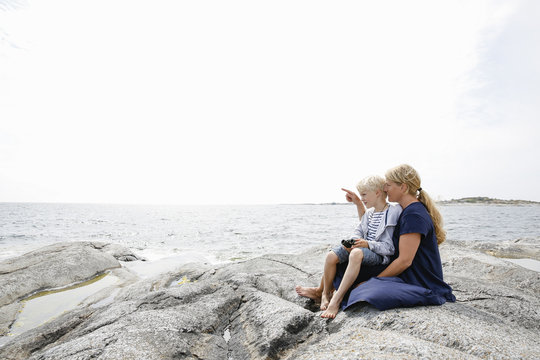 Sweden, Stockholm Archipelago, Sodermanland, Huvudskar, Mother and son (6-7) sitting on rocky seashore