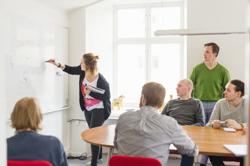 Sweden, Young woman drawing on white board during work meeting