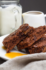 Brownie with caramel on a white plate, milk and saucepan with caramel.
