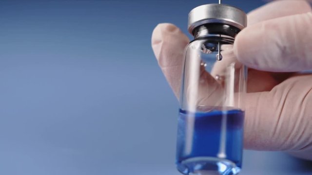 Close up shot of mixing of drug. Nurse using syringe to squirt blue fluid into ampoule.