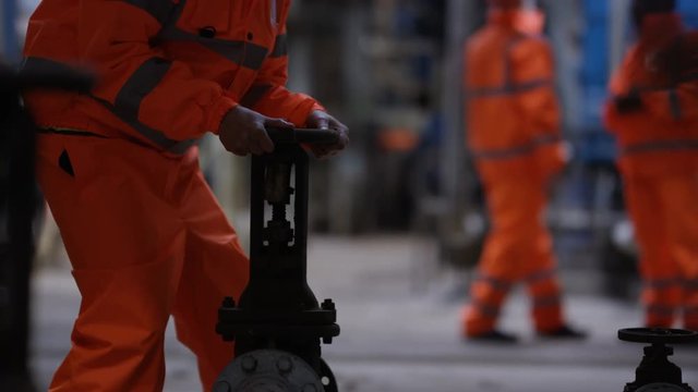  Male & female engineers in power plant turning a valve on machinery