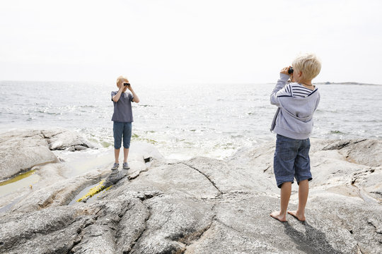 Sweden, Stockholm Archipelago, Sodermanland, Orno, Two boys (6-7, 8-9) standing on rocky seashore and looking through binoculars