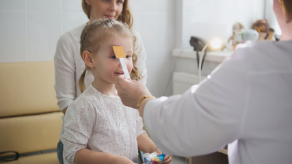Cute blonde girl with mommy in child's ophthalmology - optometrist diagnosis eyesight