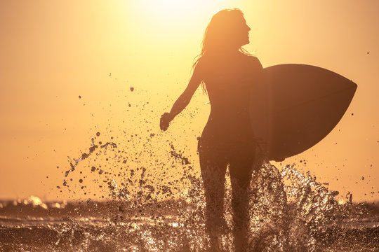 Young woman runs with surfboard with lots of splashes