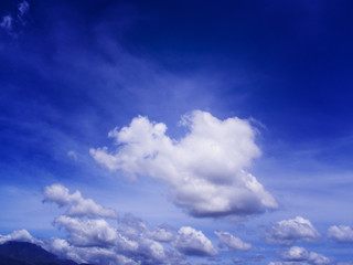 Blue sky with white fluffy cloud. Distant mountain dark silhouette on bright blue sky
