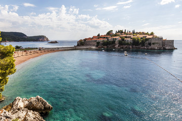 Fototapeta premium Sand beach with wooden chairs and umbrellas near the Sveti Stefan historical town on the island.