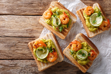 Tasty toast with guacamole, prawns and lime close-up. horizontal top view