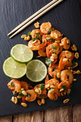 Sauteed shrimp with peanuts, lime and greens closeup on the table. vertical top view