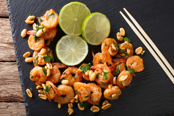 Sauteed shrimp with peanuts, lime and greens closeup on the table. horizontal top view