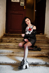 Young goth girl on black leather skirt and jacket posed on stairs of old house.
