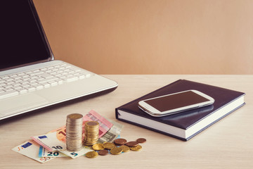 Euro money, mobile phone with notebook and laptop on the table.