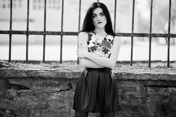 Young goth girl on black leather skirt against iron fence.