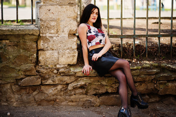 Young goth girl on black leather skirt and high heels punk shoes posed against iron fence.