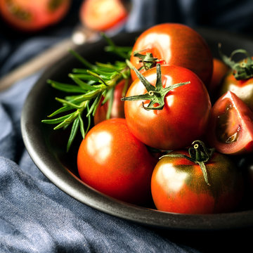 Black prince heirloom tomatoes in a black bowl with fresh rosemary sprig