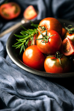 Black prince heirloom tomatoes in a black bowl with fresh rosemary sprig
