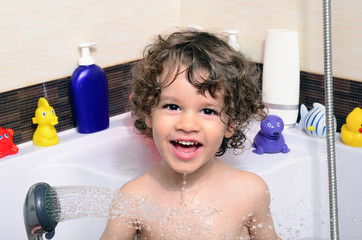 Beautiful toddler taking a bath in a bathtub with bubbles. Cute kid washing his hair with shampoo in the shower and splashing water everywhere. Boy playing with toys in the tub © iulianvalentin