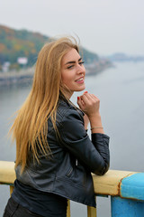 Fototapeta na wymiar Nice pretty blond hair young girl european and american race student walk in city in leather jacket, reflects on life, proper facial features blue eyes, long hair and windy weather in outdoors