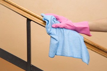 Hand in pink protective glove with rag wiping wooden staircase railing. Early spring cleaning or regular clean up. Maid cleans house.