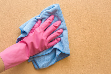 Hand in pink protective glove cleaning wall from dust with rag. Early spring cleaning or regular...