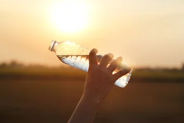 Poster hand holding drinking water on sunset background © ipopba