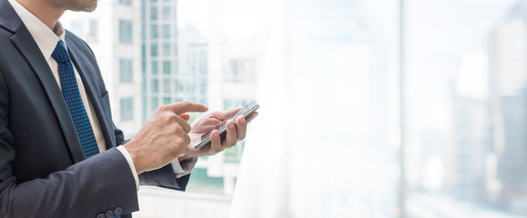 Business man using smart phone on window with city building banner background and copy space.