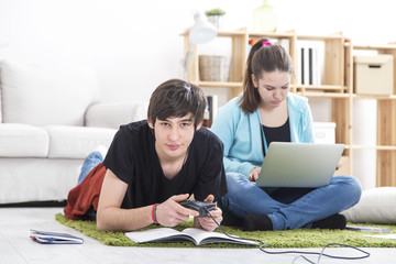 Two teenage friend. Boy playing game console, girl working on laptop