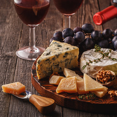 Cheese, nuts, grapes and red wine on wooden background.