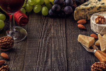 Fototapeta premium Cheese, nuts, grapes and red wine on wooden background.