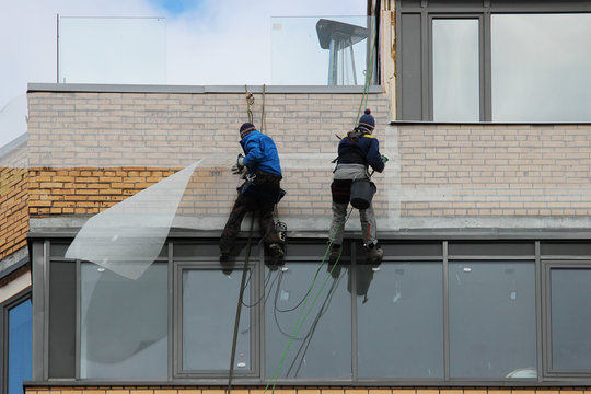 Industrial climbers fix a building mesh on the wall of a tall building