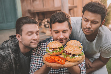 Three young men with closed eyes sniffing fresh homemade hamburgers